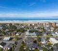 Aerial view of a coastal neighborhood with sandy beaches and ocean waves just beyond tree-lined residential streets and nearby buildings.