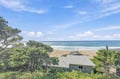 The property sits just steps from sandy shores where gentle waves meet the beach, surrounded by coastal greenery and open skies.