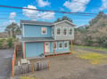 A charming two-story coastal home featuring blue siding and modern design, nestled among mature trees in a peaceful residential setting.
