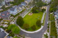 Aerial view of a charming coastal neighborhood with colorful homes, tree-lined streets, and a central park featuring playground equipment.