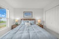Settle into your peaceful retreat with plush bedding, warm bedside lighting, and a calming coastal-inspired view framed above the woven headboard.