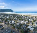 An aerial view captures a charming coastal community nestled between forested hills and pristine sandy shores, with the endless Pacific stretching beyond gentle waves.