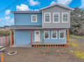 Charming two-story coastal home with blue siding and spacious front porch, perfect for a peaceful getaway retreat.