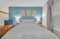 Rest peacefully in your serene bedroom with calming blue accent wall, crisp linens, and warm bedside lighting.