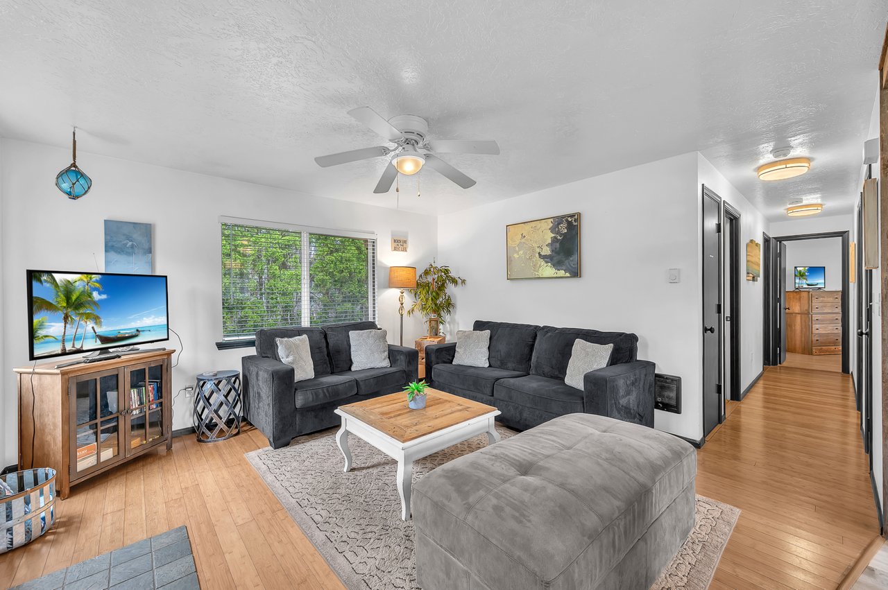 Relax in your spacious living room with plush sofas, a large TV, and cool ceiling fan. Bright windows and coastal décor set the stage for your perfect getaway.