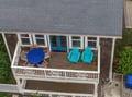 Aerial view of the property exterior featuring a spacious multi-level deck with outdoor seating, bright turquoise Adirondack chairs, and a blue dining table—the perfect setup for enjoying coastal breezes and relaxed outdoor living.
