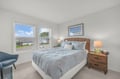 Your serene bedroom retreat features soft coastal tones, a plush woven headboard, and bright windows inviting natural light—perfect for peaceful mornings and restful nights.