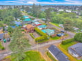 Aerial view of the property and surrounding residential neighborhood with tree-lined streets and coastal landscape beyond.