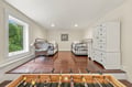Spacious bedroom with gleaming hardwood floors, twin beds, white dresser storage, and a cozy wicker chair by the bright window. Foosball table adds playful fun.