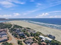 Aerial view of a coastal neighborhood nestled between the ocean and a tranquil bay, surrounded by sandy shores and natural beauty.