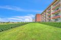 Multi-story property buildings surrounded by well-maintained green lawns and landscaping under a bright blue sky.