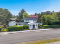 Charming white property nestled among lush trees and colorful gardens in a peaceful residential neighborhood.